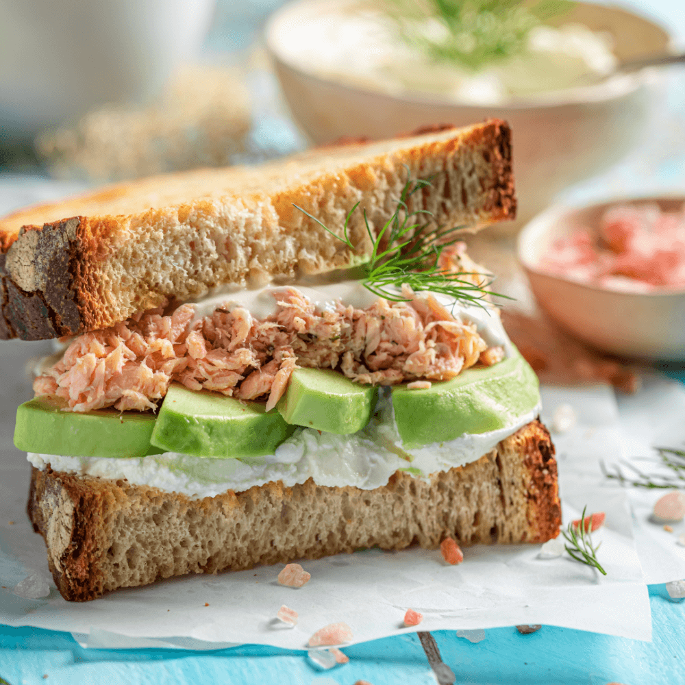 A fresh sandwich with avocado, salmon, and cream cheese on thick toasted bread, garnished with dill. - Home Instead