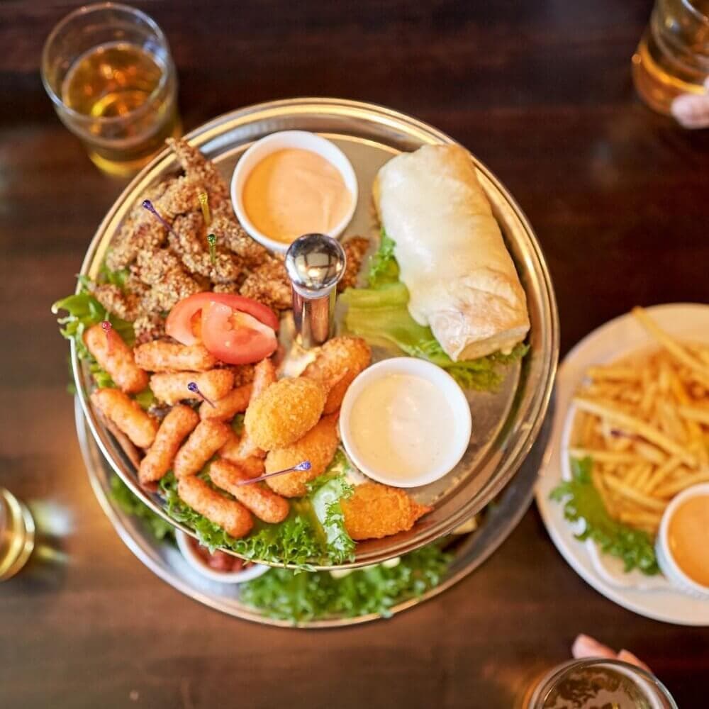 Aerial view of a platter with appetizers, including crispy rolls, fried items, and dips; sides of fries and drinks. - Home Instead