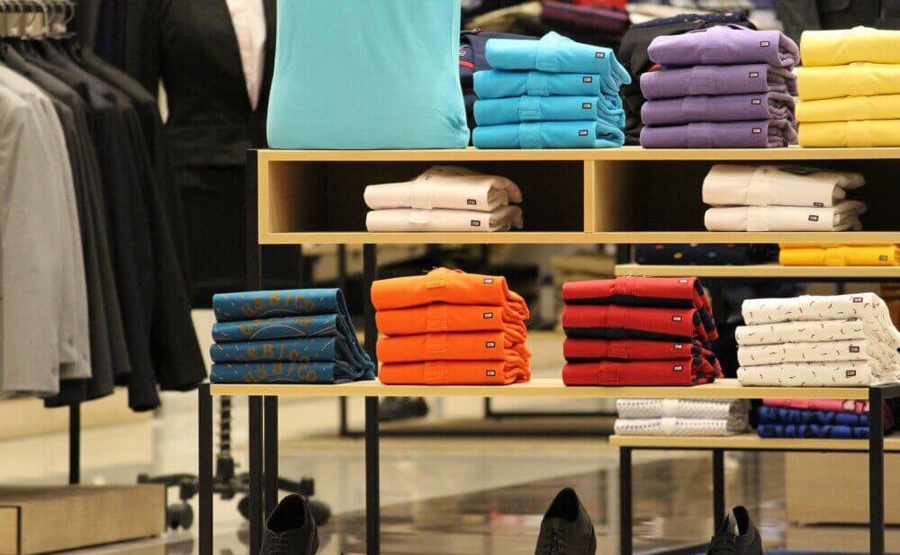 A display in a retail store showcasing neatly folded shirts in various colors, with shoes at the bottom. - Home Instead