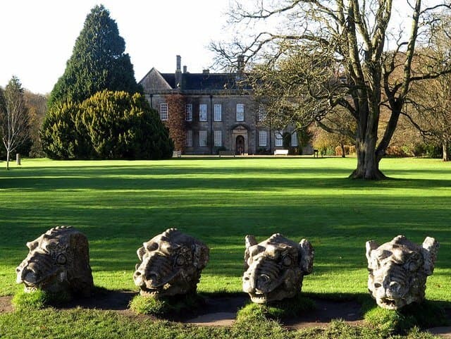 Stone animal head sculptures in front of a large historic building surrounded by a green lawn and trees. - Home Instead