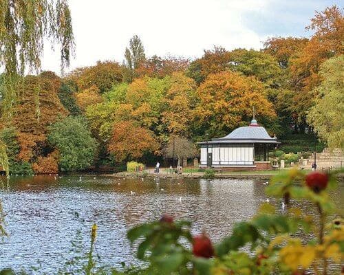 A serene lake with a gazebo surrounded by autumn trees, and some people walking along the shoreline. - Home Instead