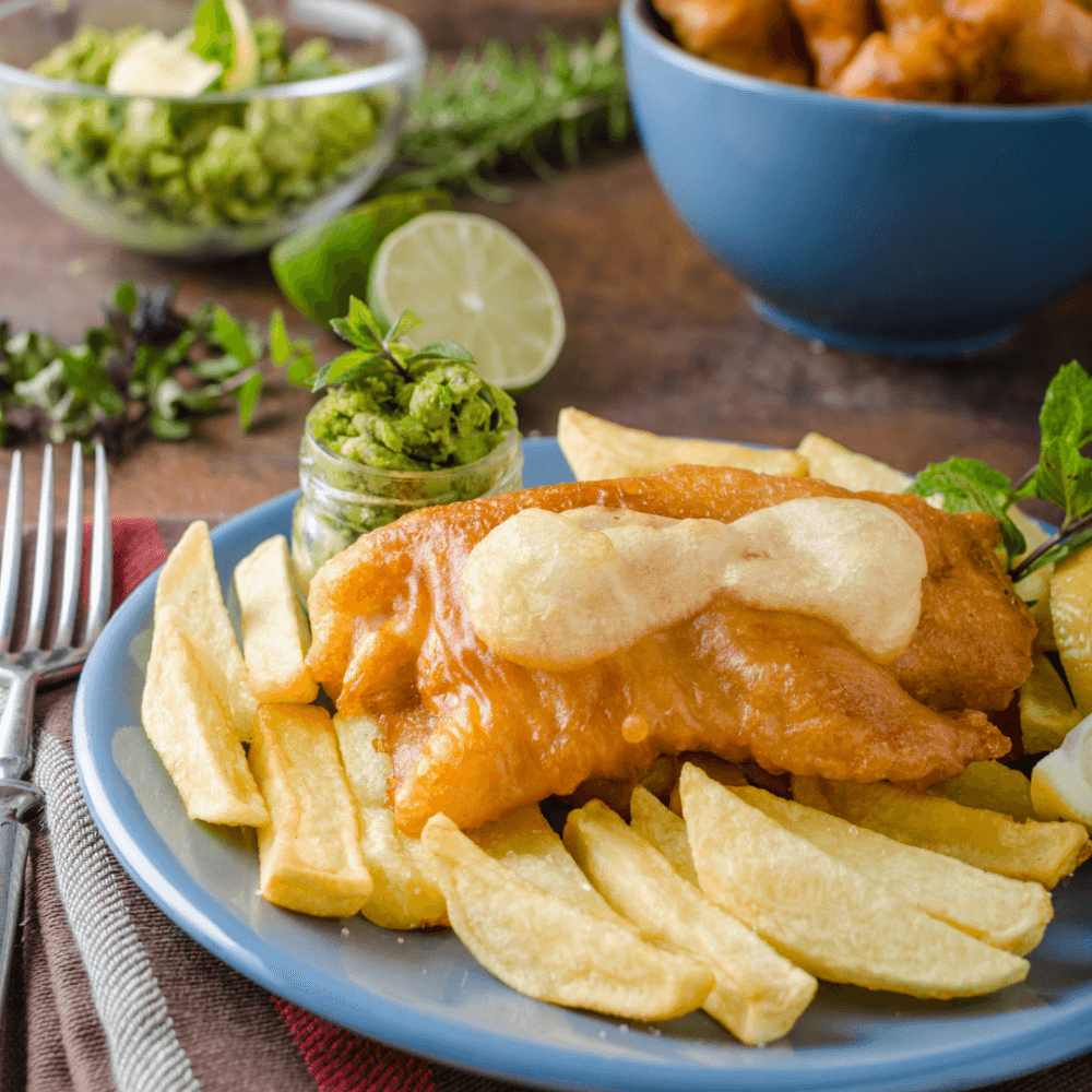 A plate of fish and chips with a dollop of sauce, a lime wedge, and a small side of guacamole. - Home Instead