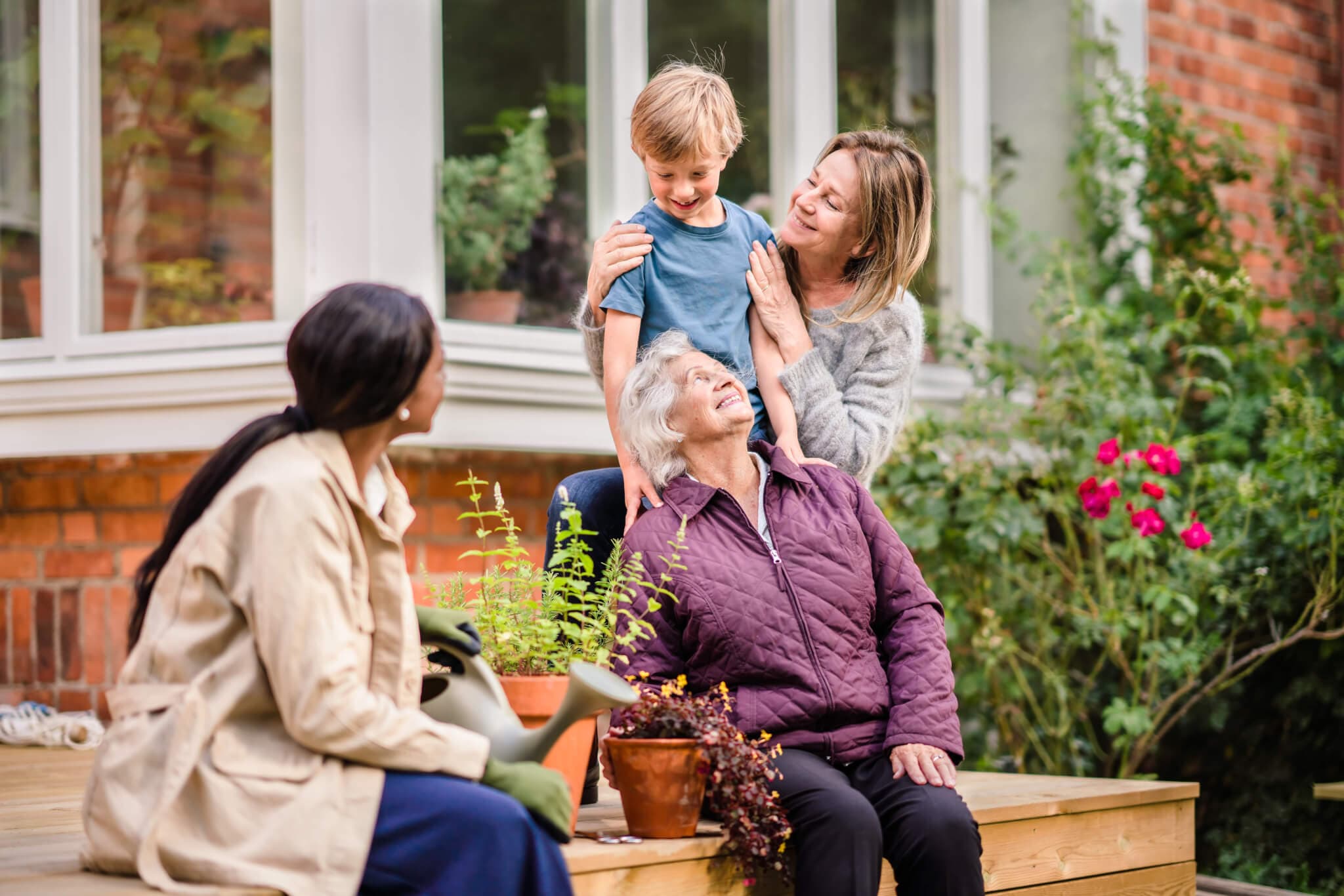 Four people of different ages enjoying time together outdoors, surrounded by plants and flowers. - Home Instead
