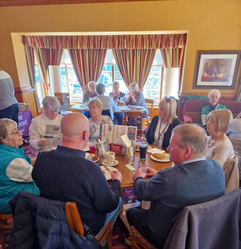 A group of elderly people are sitting around a table in a cozy dining room, conversing and reading newspapers. - Home Instead