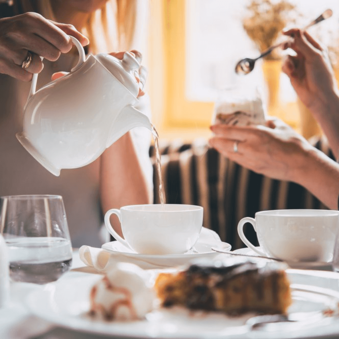 Two people enjoying tea at a well-lit table, with teacups and pastries in front of them. - Home Instead