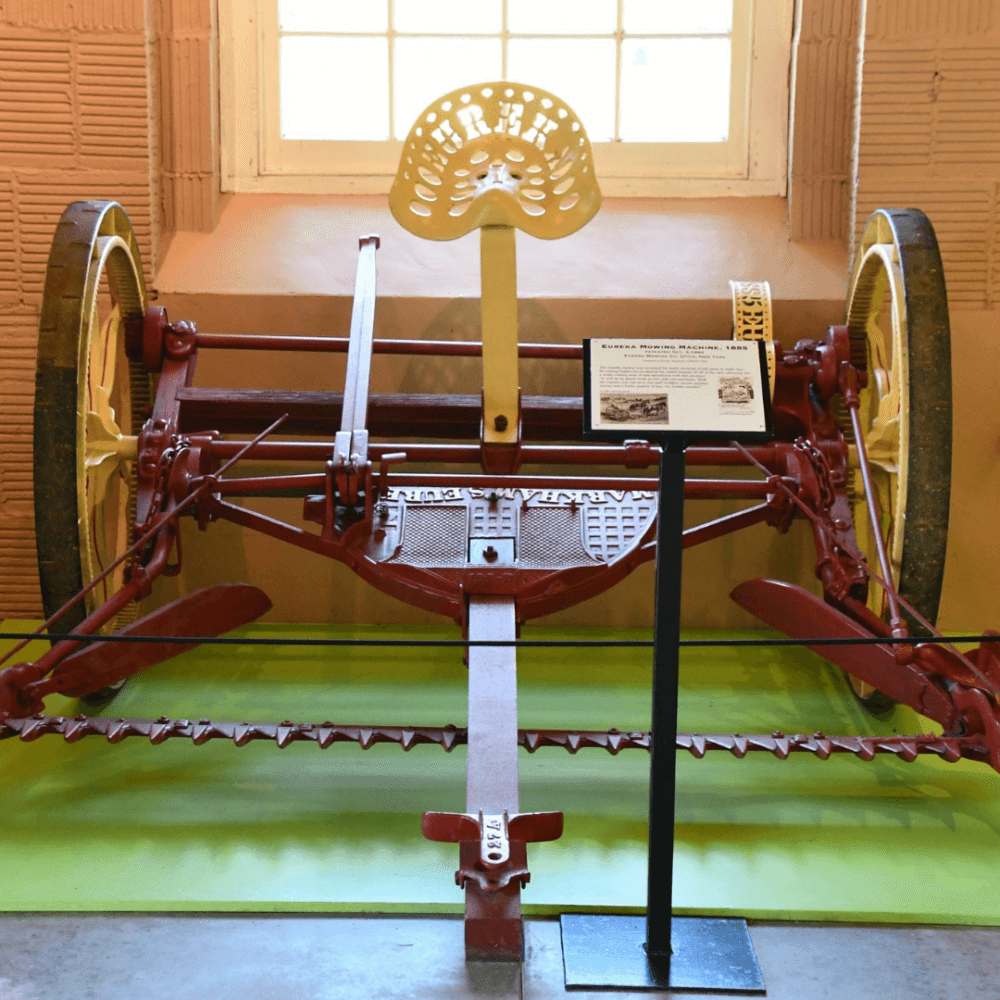 An antique red and yellow agricultural machine displayed indoors with an information plaque in front of it. - Home Instead