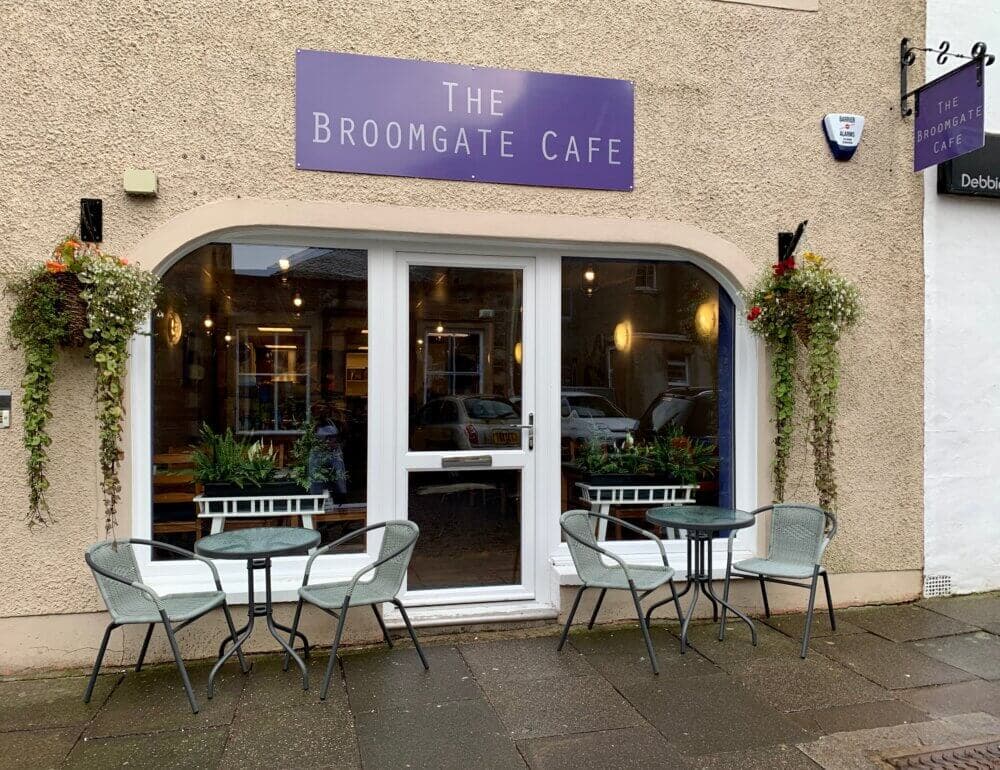 A quaint cafe with outdoor seating and a sign reading "The Broomgate Cafe" above the door. - Home Instead