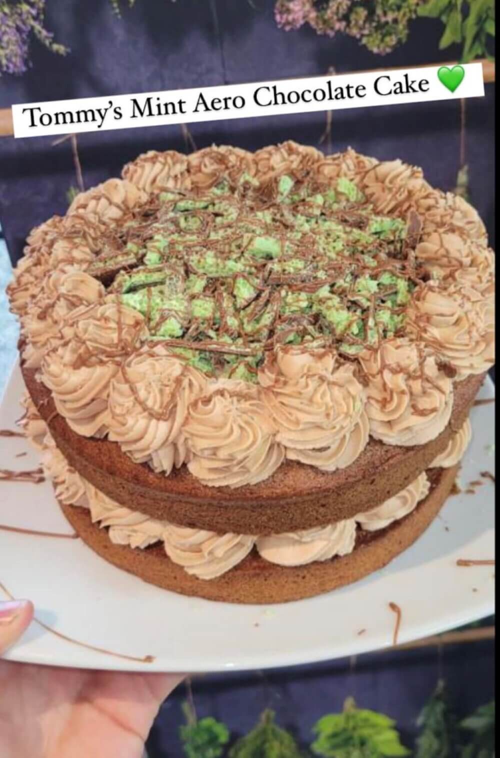 A double-layer chocolate cake with mint Aero pieces on top and chocolate frosting, labeled "Tommy's Mint Aero Chocolate Cake. - Home Instead