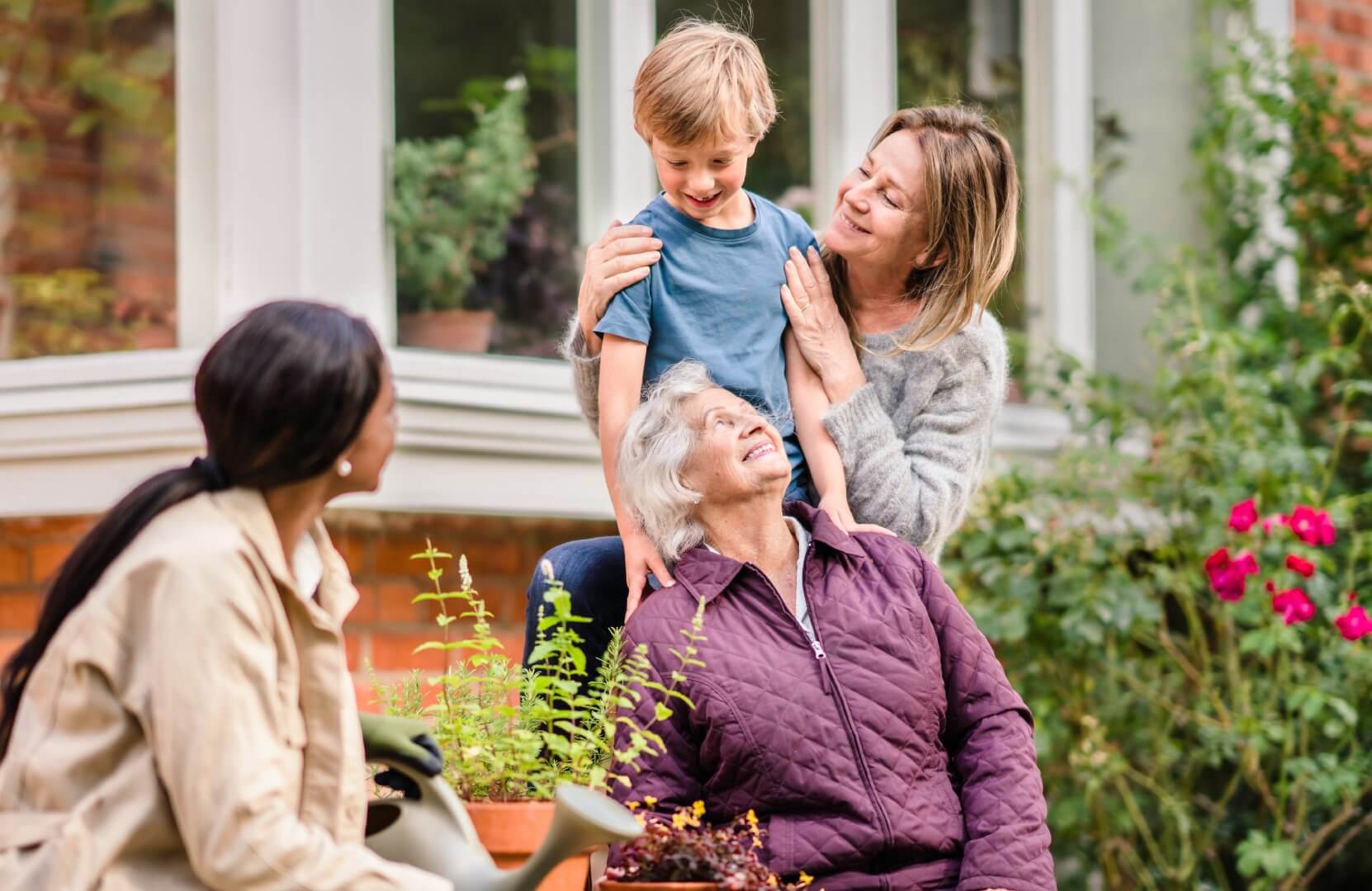 Four people, including a child and seniors, enjoying a garden together and smiling warmly. - Home Instead