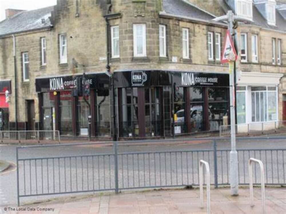 Street view of Kona Coffee House on the ground floor of a stone building with large windows and black signage. - Home Instead