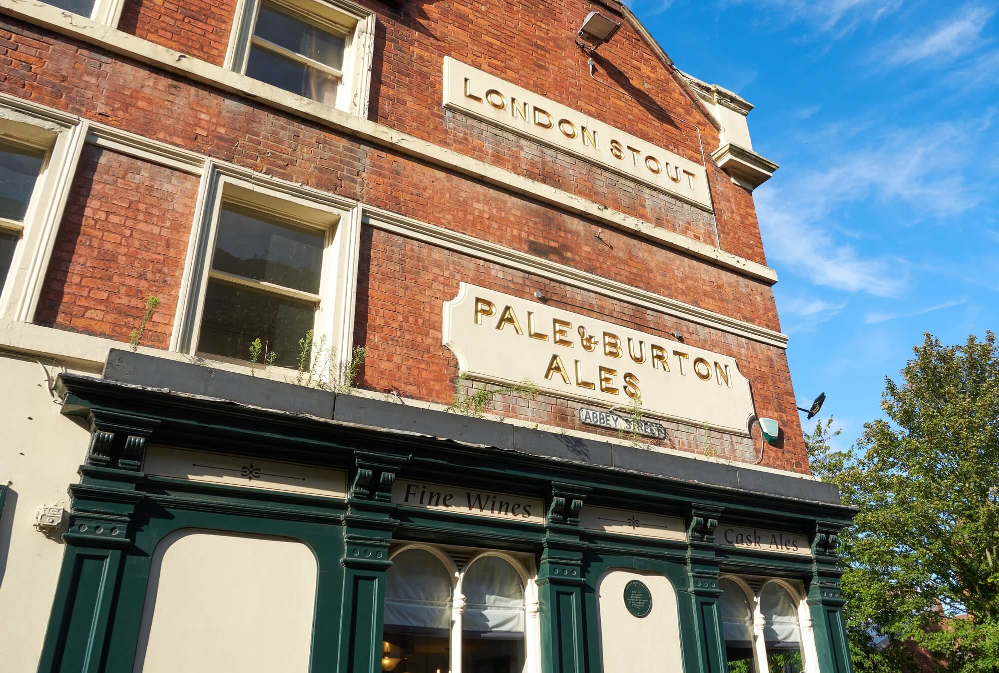 Old brick building with signs reading "LONDON STOUT" and "PALE & BURTON ALES" on a sunny day. - Home Instead