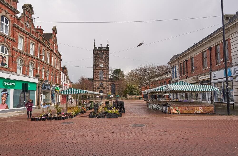Empty market stalls in a town square with surrounding historic buildings and a clock tower in the background. - Home Instead