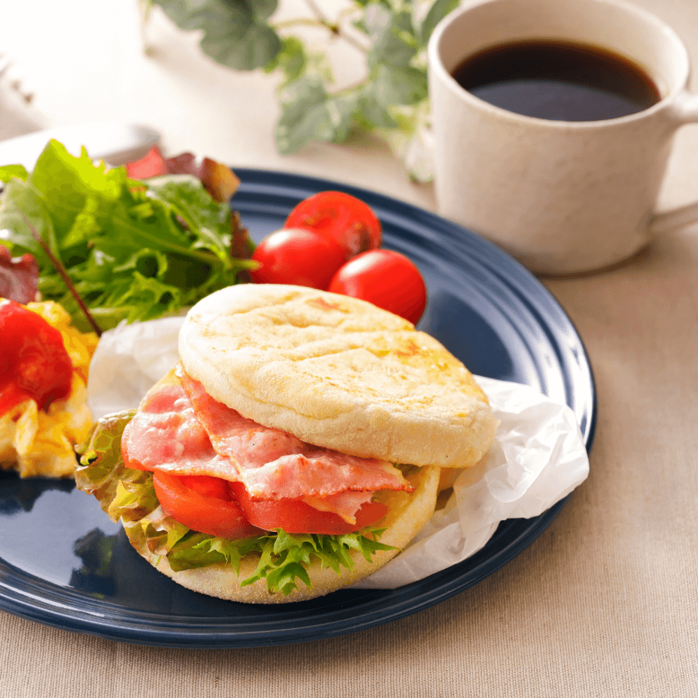 A breakfast sandwich with lettuce, tomato, and bacon on a blue plate, served with a salad and a cup of coffee. - Home Instead