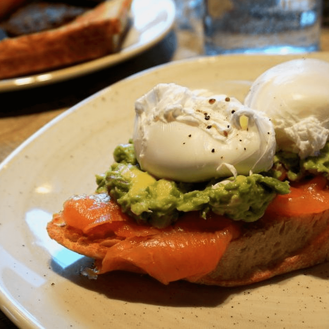 Toast topped with avocado, smoked salmon, and two poached eggs on a ceramic plate. - Home Instead
