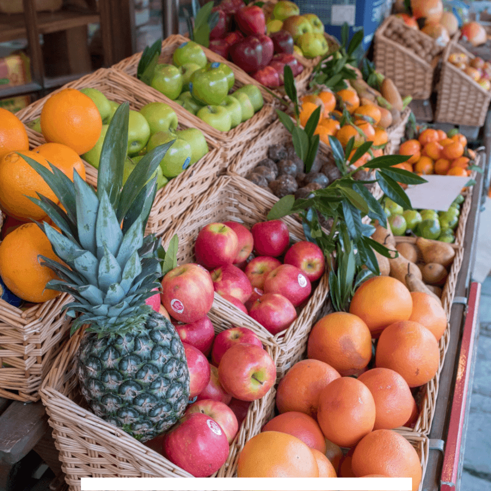 Assorted fruits in wicker baskets on display at a market, including apples, oranges, pineapple, and other fresh produce. - Home Instead