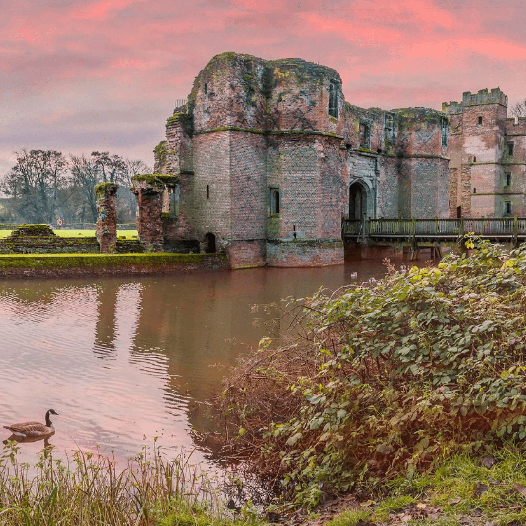 Medieval castle ruins beside a moat with a duck swimming, under a vibrant pink sky at sunset. - Home Instead