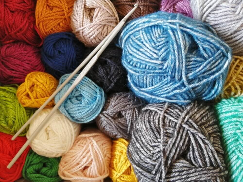 A variety of colorful yarn balls arranged with two knitting needles resting on top. - Home Instead