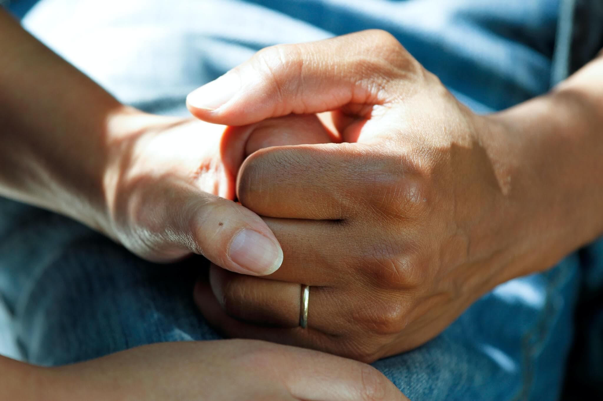 Two hands holding each other gently, with a gold band on one finger, highlighting support and care. - Home Instead