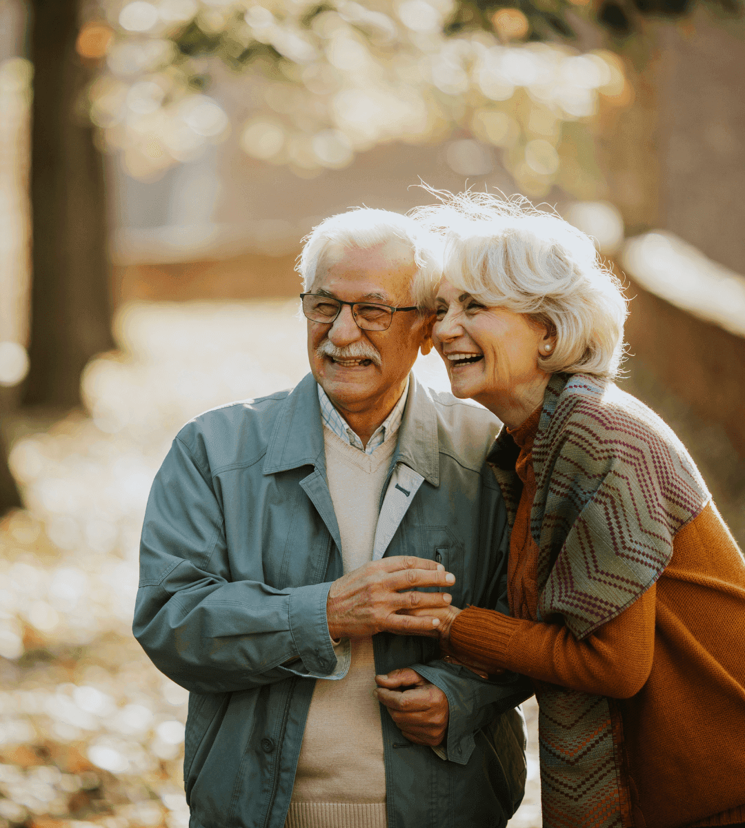 Elderly couple smiling and walking together in a park during autumn. - Home Instead