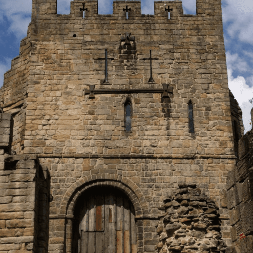 A stone castle entrance with a large wooden door and battlements under a partly cloudy sky. - Home Instead