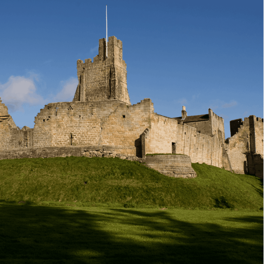 Ruins of an old stone castle on a green grassy hill with a bright blue sky in the background. - Home Instead