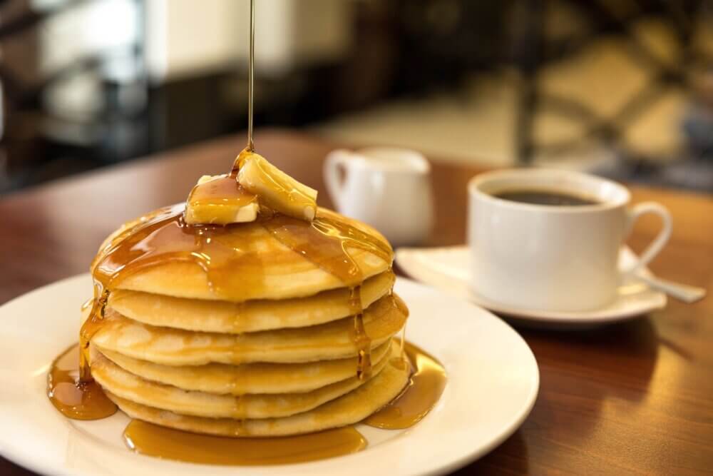 Stack of pancakes topped with butter and syrup, with a cup of coffee in the background. - Home Instead