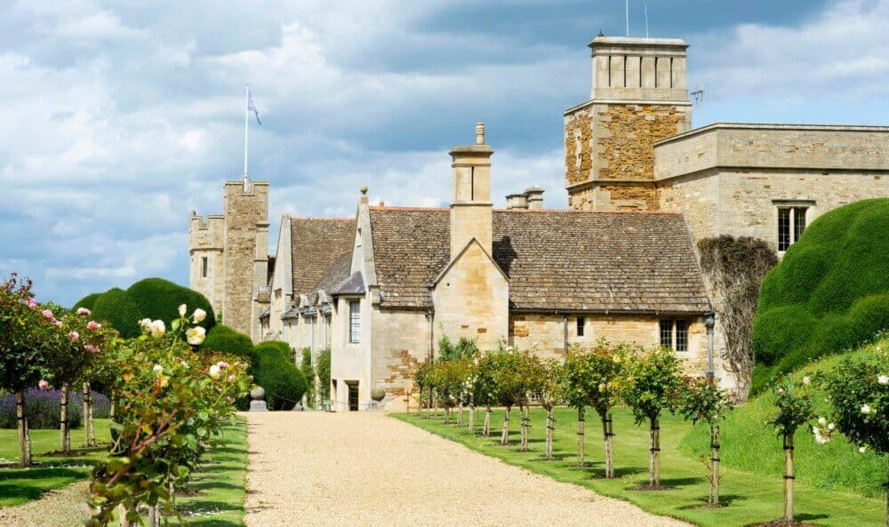 Historic stone building with turrets, manicured gardens, and a gravel path under a cloudy sky. - Home Instead