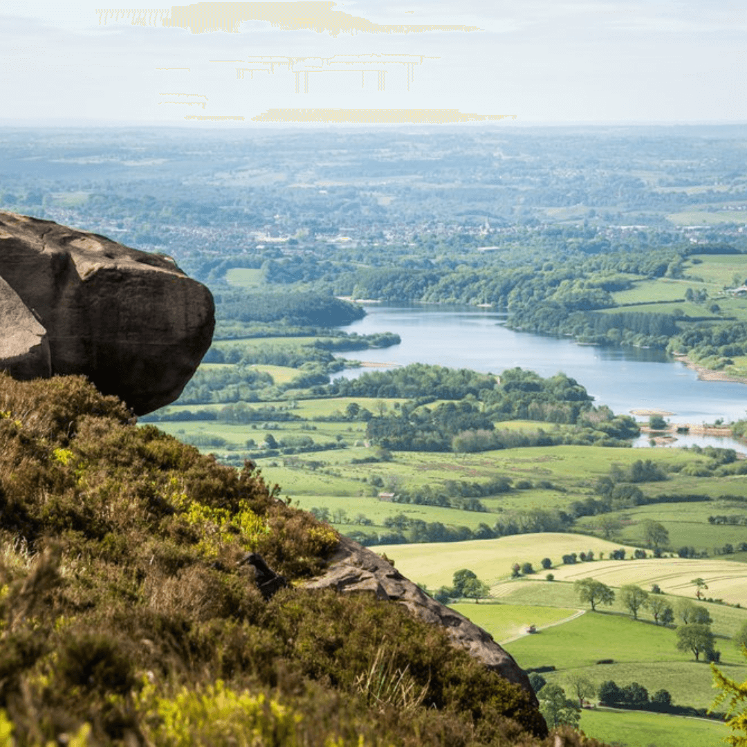 A scenic view from a rocky hill overlooking a lush green landscape with a river and distant horizon. - Home Instead