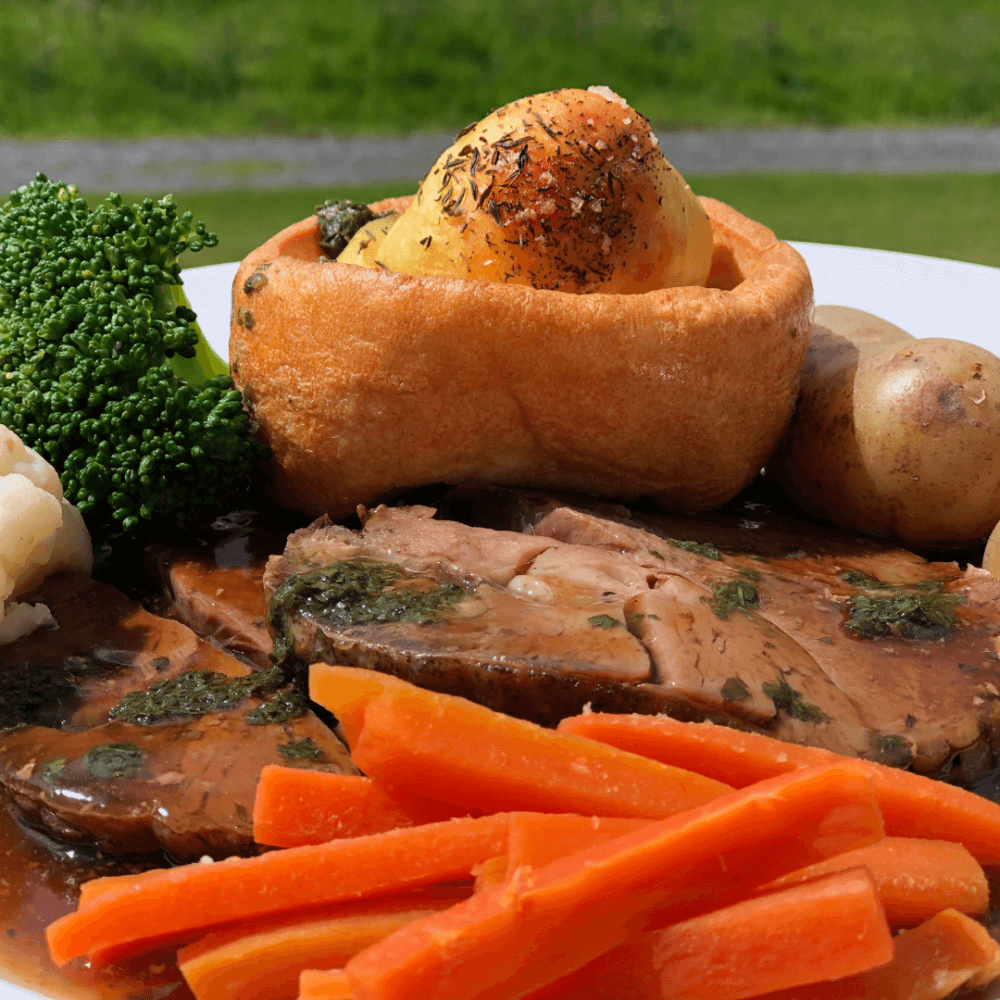 A plate of roast beef with gravy, roasted potatoes, Yorkshire pudding, carrots, broccoli, and cauliflower. - Home Instead