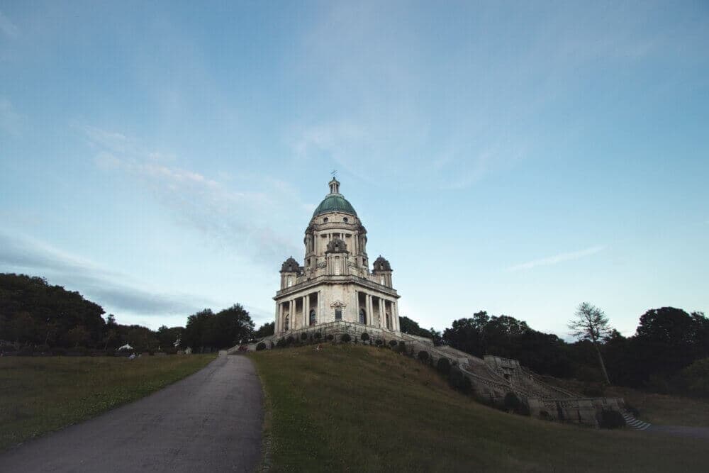 A historical building with a dome on a grassy hill, surrounded by trees under a clear blue sky. - Home Instead