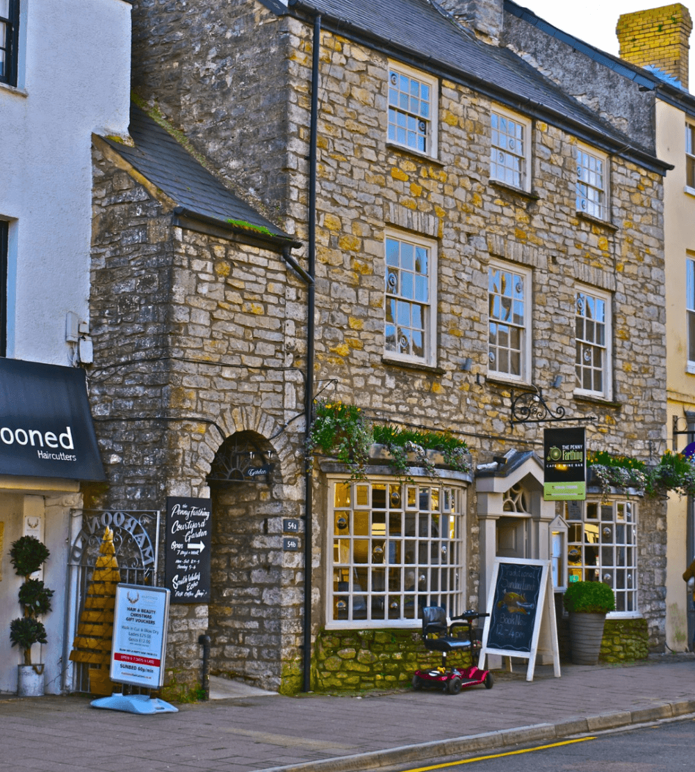 Street view of a charming stone building with a retail shop and various signs on the sidewalk. - Home Instead