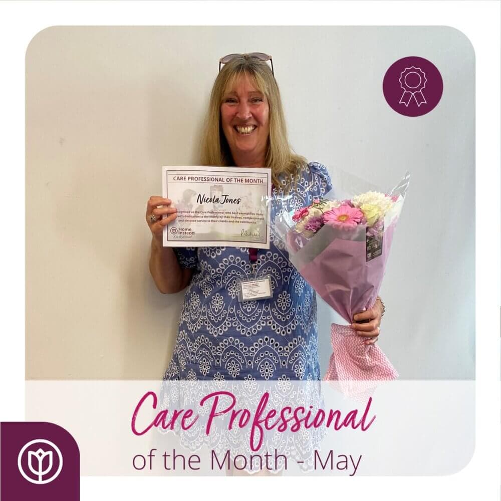 A woman smiling, holding flowers and a certificate for "Care Professional of the Month - May. - Home Instead