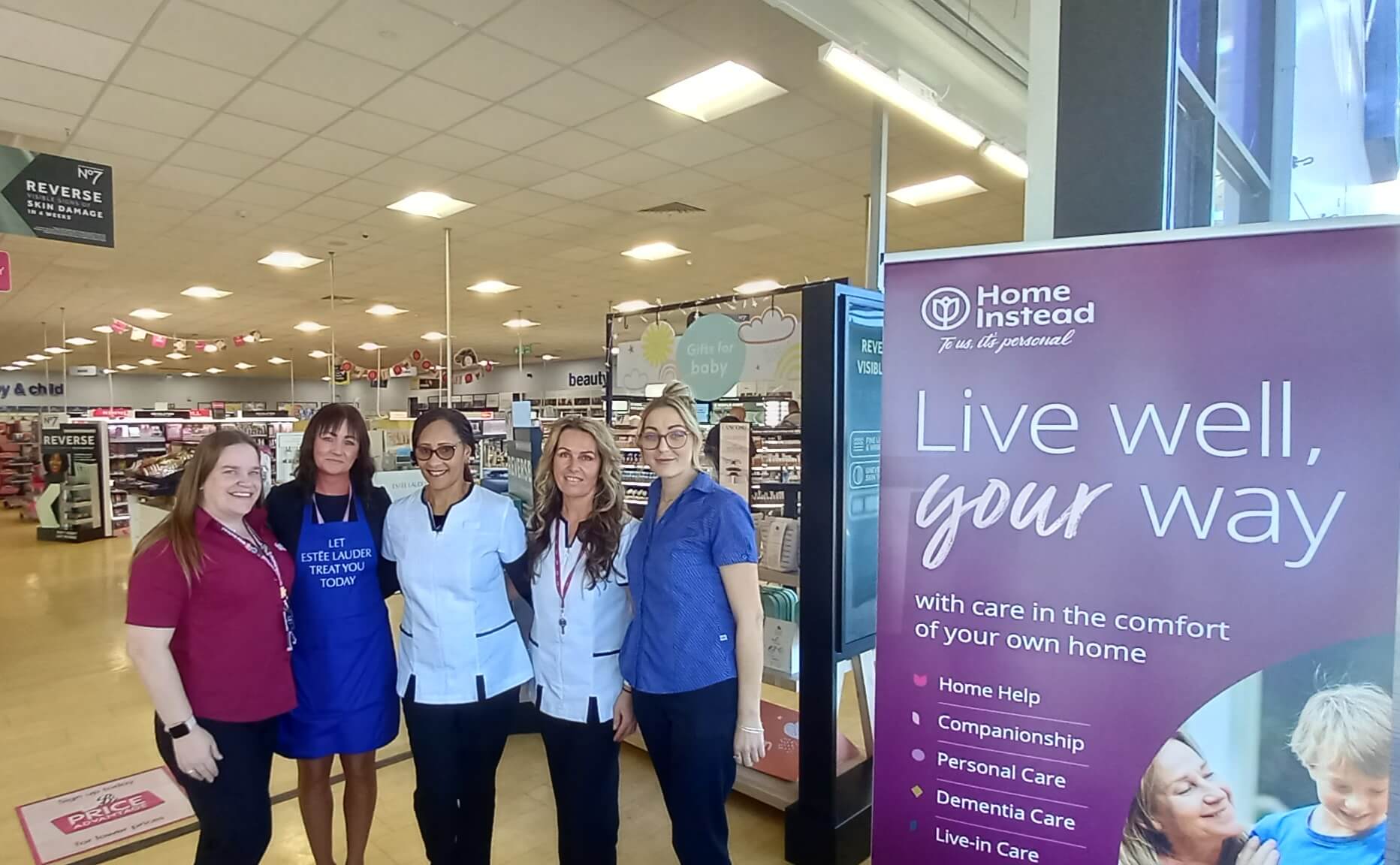 Five people standing near a "Home Instead" banner in a store aisle, promoting home care services. - Home Instead