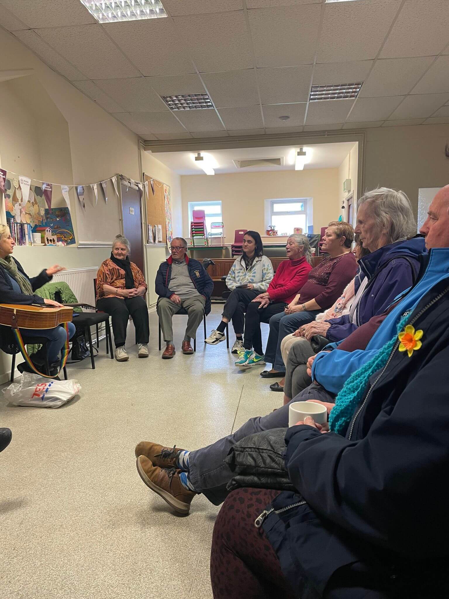 A group of people sit in a circle in a room, engaged in a discussion, with one person gesturing while speaking. - Home Instead