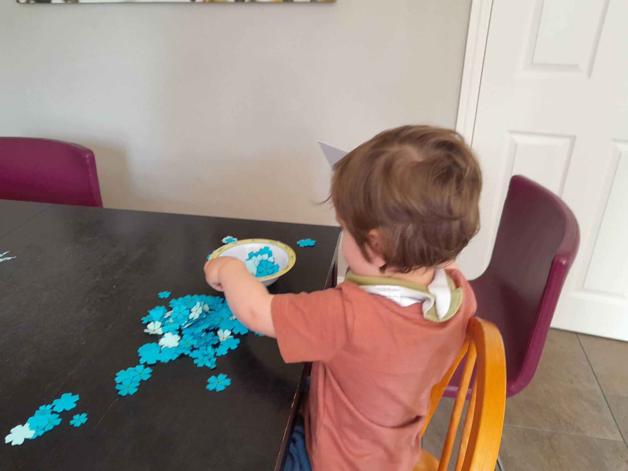 Child seated at a table, playing with blue puzzle pieces. - Home Instead