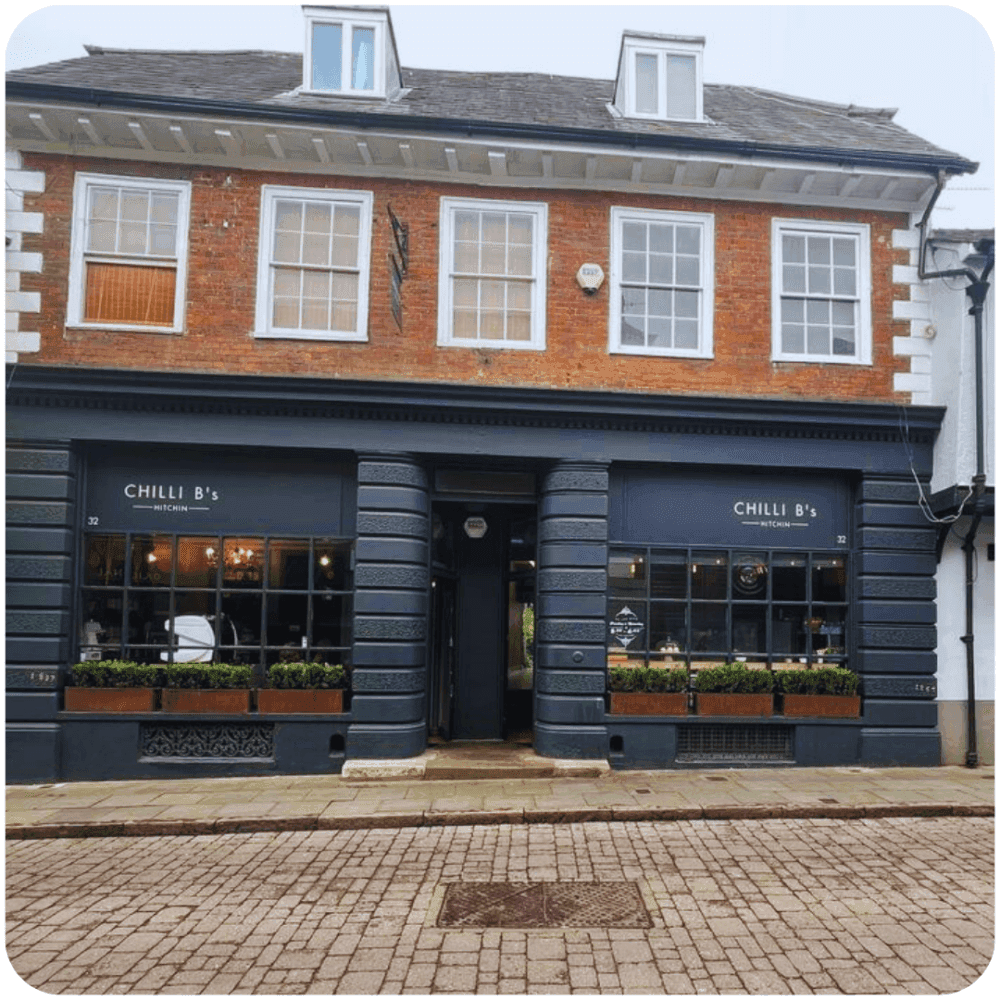 A two-story building with a storefront labeled "Chilli B's" on a cobblestone street. - Home Instead