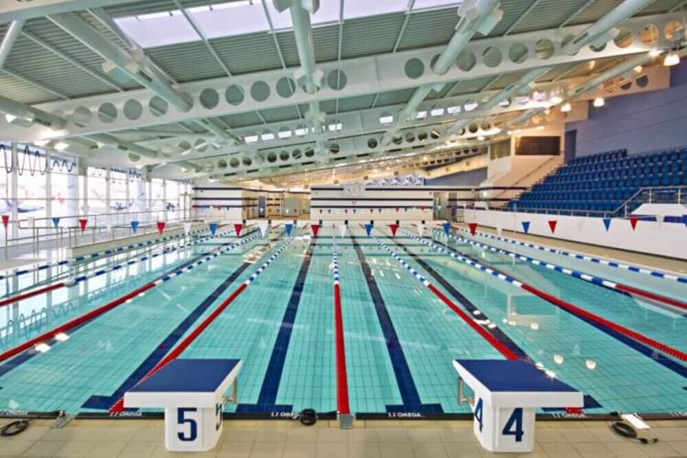 Indoor swimming pool with lanes marked, starting blocks numbered 4 and 5, and spectator seating in the background. - Home Instead