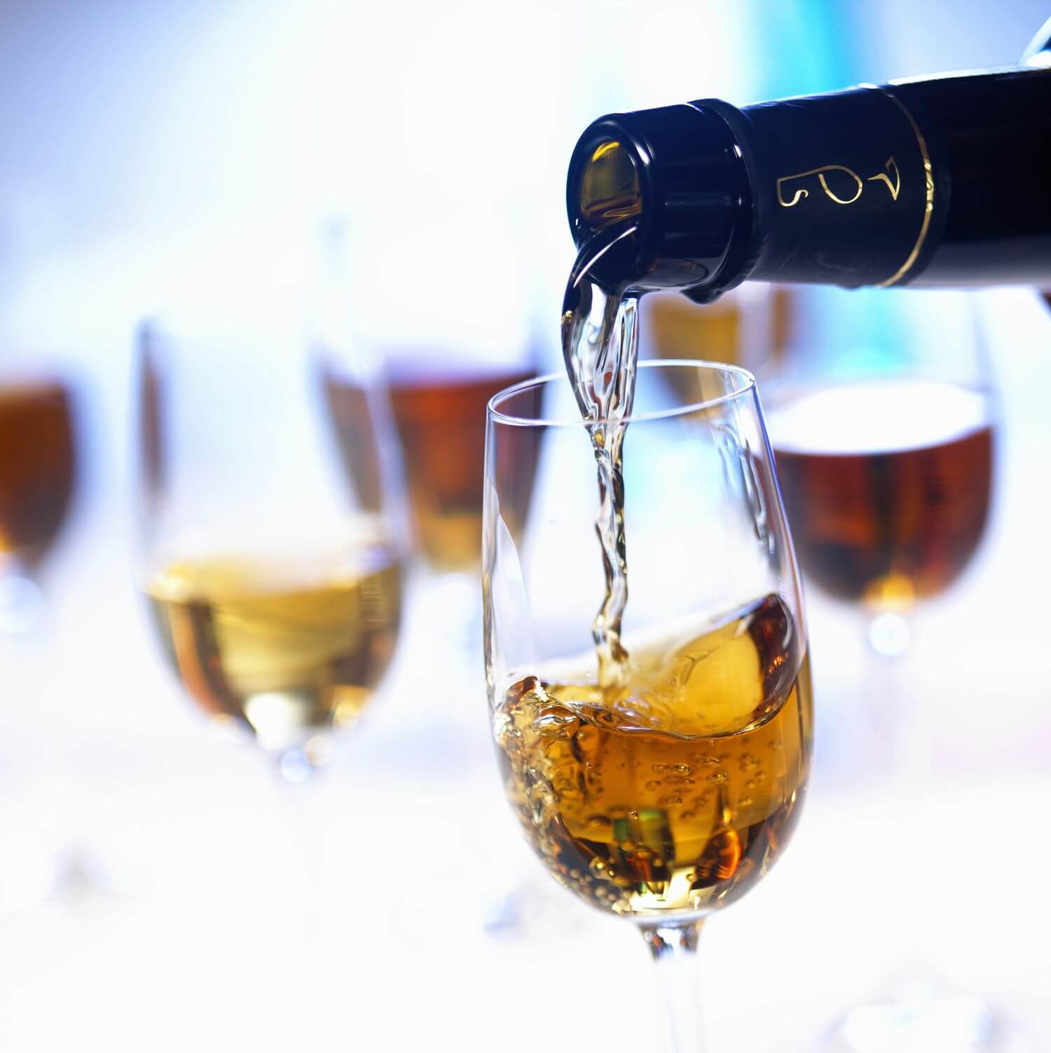 Close-up of a bottle pouring golden liquid into a wine glass, with similar filled glasses visible in the background. - Home Instead