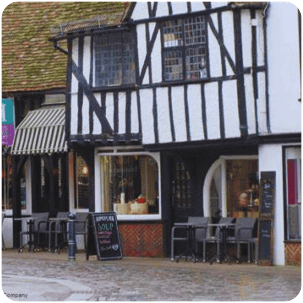 A charming Tudor-style café with outdoor seating and a sandwich board advertising soup, located on a cobblestone street. - Home Instead
