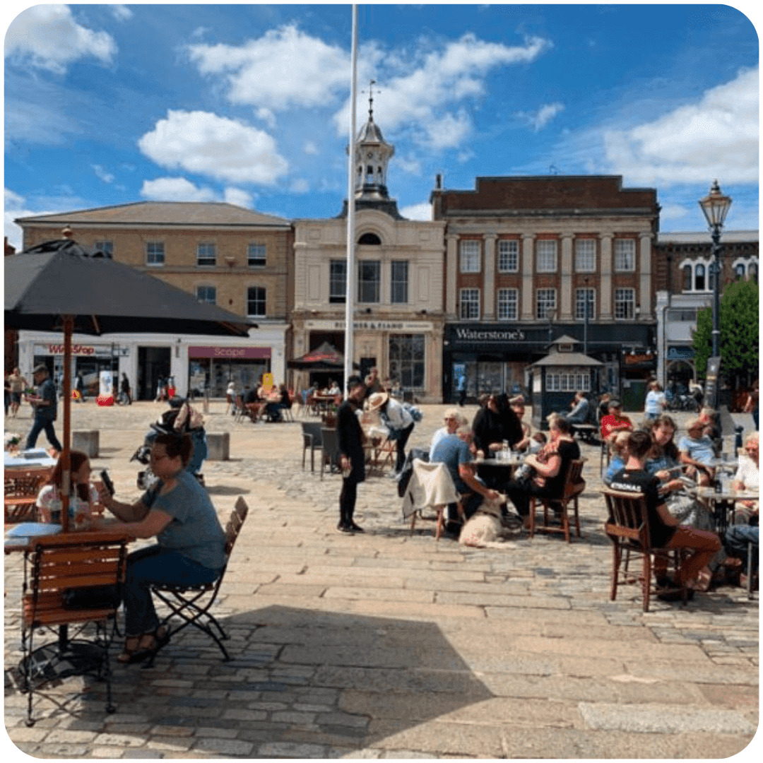 Outdoor cafe with several people dining and chatting on a sunny day in a town square with historic buildings. - Home Instead