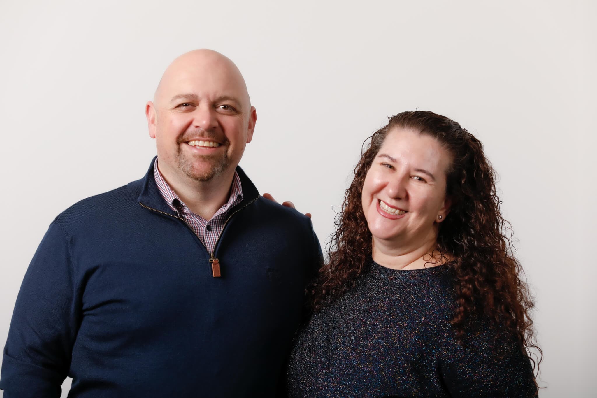 A man and a woman smiling, standing close together against a plain white background. - Home Instead