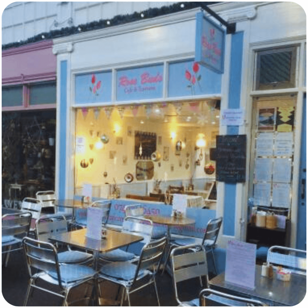 Outdoor seating area of a cozy cafe with blue and white facade, named "Rose Buds Cafe & Bakery. - Home Instead
