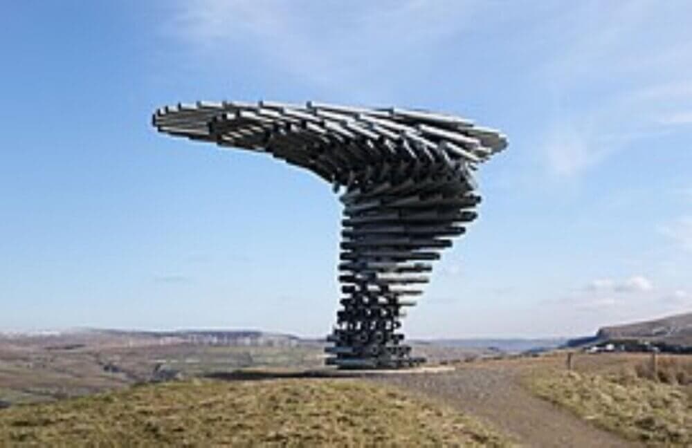 The image shows the Singing Ringing Tree, a wind-powered sound sculpture on a hilltop under a clear sky. - Home Instead