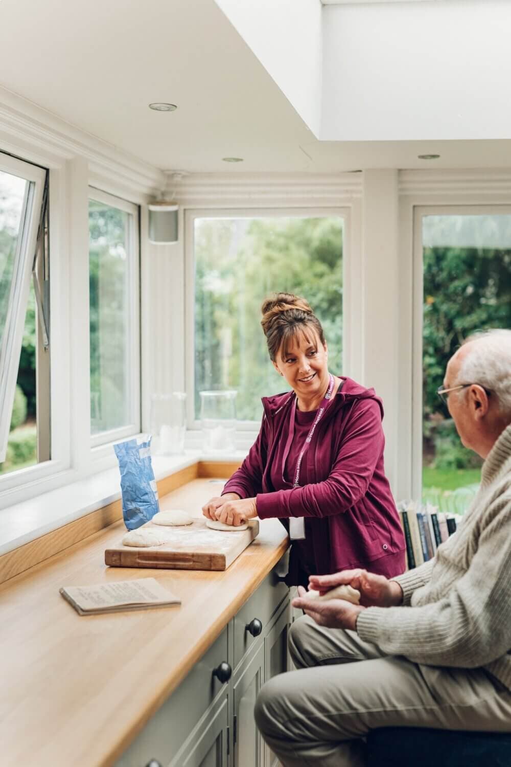 A woman and an elderly man engage in a conversation by a window in a bright kitchen with wooden countertops. - Home Instead
