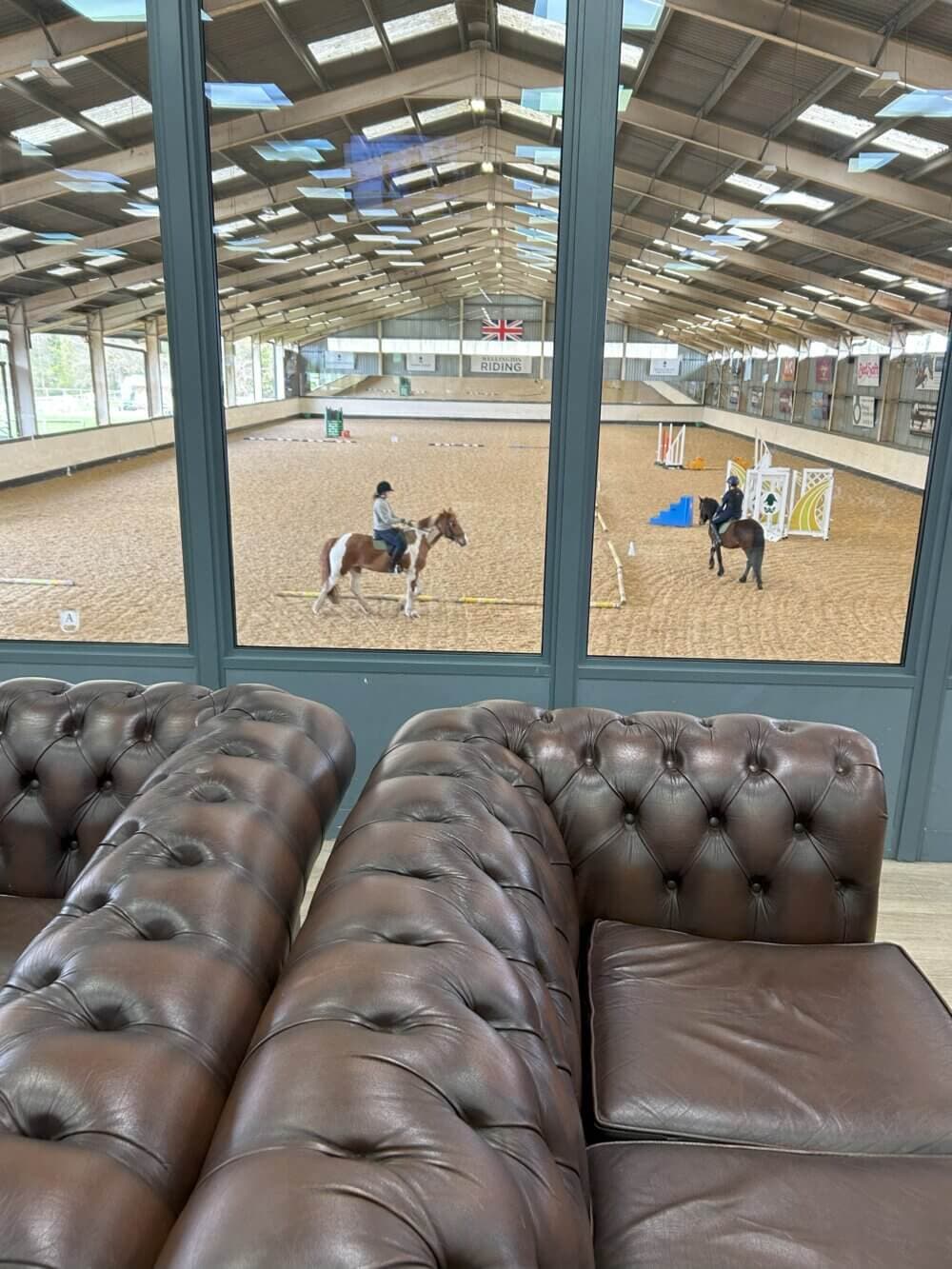 Home Instead Basingstoke picture of two horses being ridden at Wellington Riding Stables indoor equestrian arena, near Basingstoke.