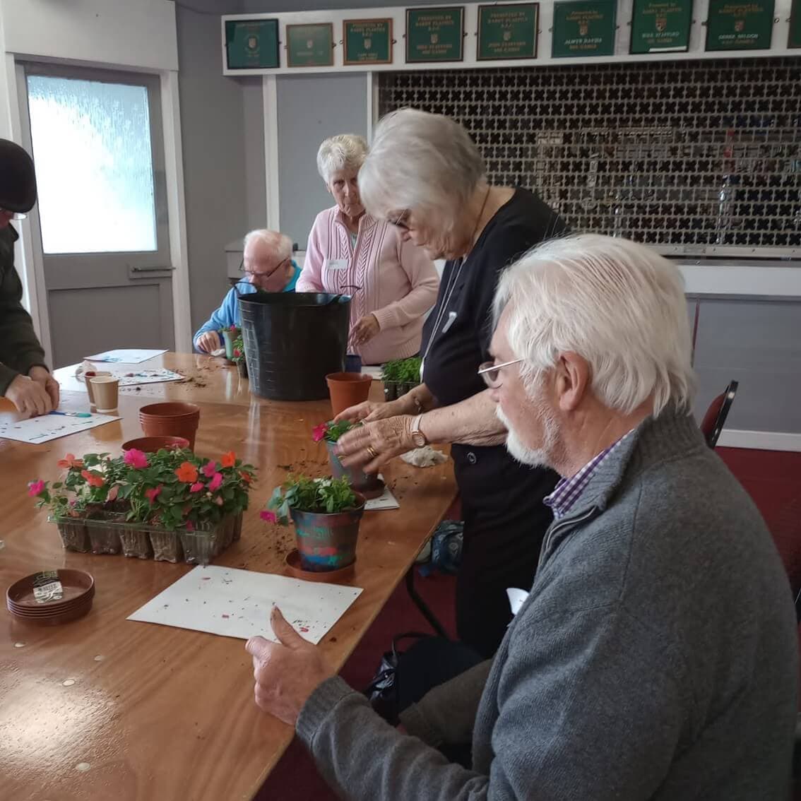 A group of elderly individuals working with plants together at a table indoors. - Home Instead
