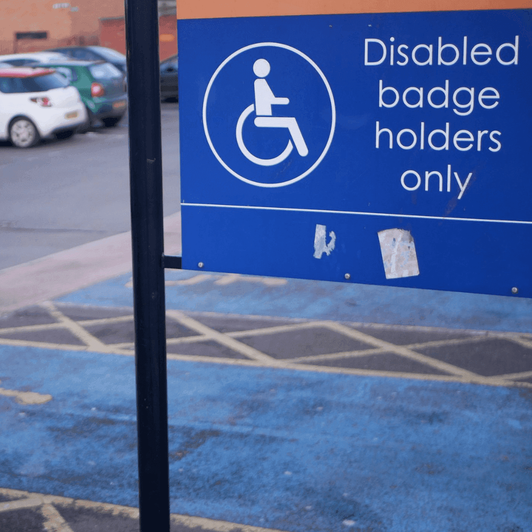 Sign in a parking lot designating spaces for disabled badge holders only, with blue markings on the ground. - Home Instead