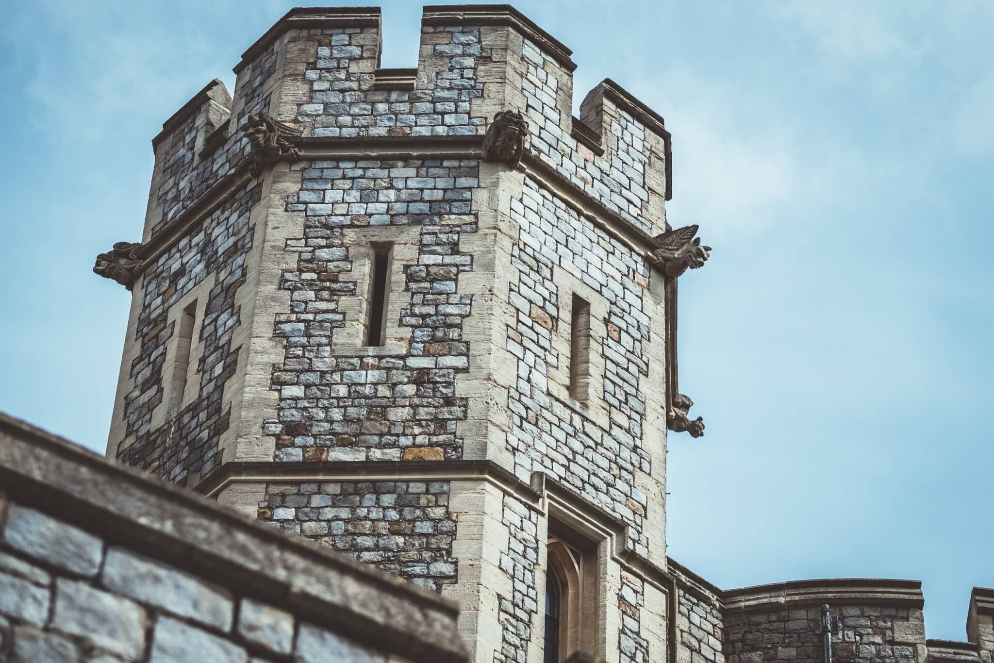 Stone castle turret with crenellations and narrow windows against a blue sky. - Home Instead