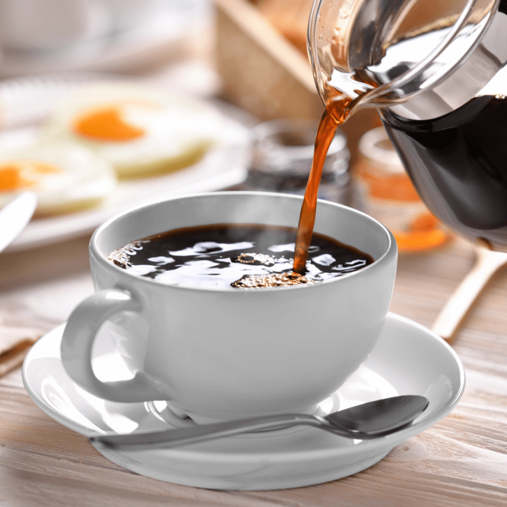 A cup of coffee being poured from a glass pot, with breakfast items blurred in the background. - Home Instead
