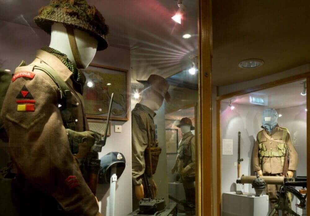 Museum display featuring three WWII-era military uniforms and various equipment in a glass case. - Home Instead